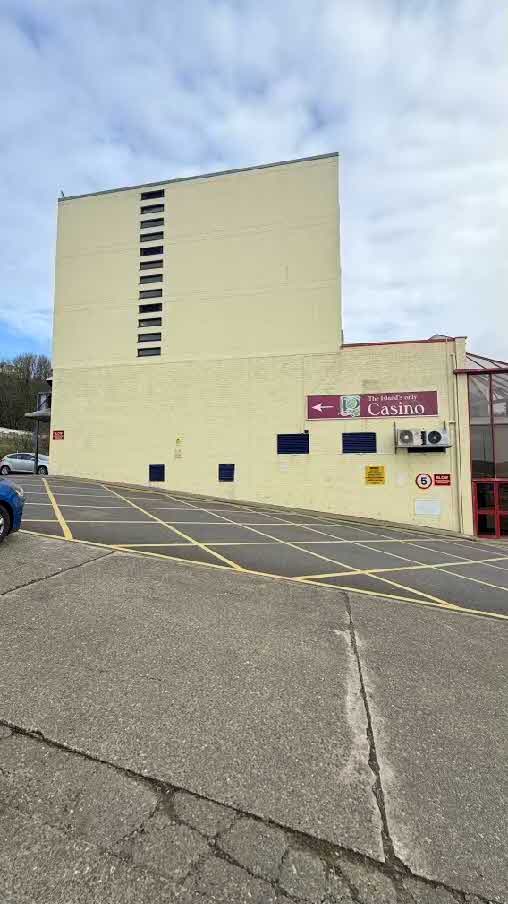 A photograph showing the cream-colored exterior wall of a commercial building, likely the Best Western Palace Hotel, viewed from an adjacent car park with yellow road markings.