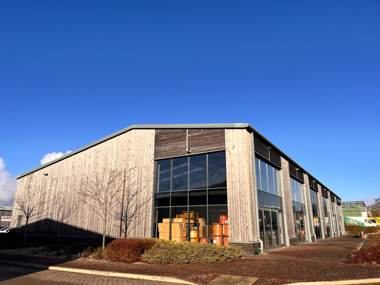 A low-angle photograph of a large, modern industrial building featuring light wood cladding and extensive glass windows under a clear blue sky.