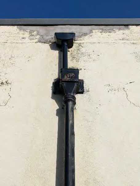 A close-up photograph showing a black drainpipe and junction box attached to a white rendered exterior wall.