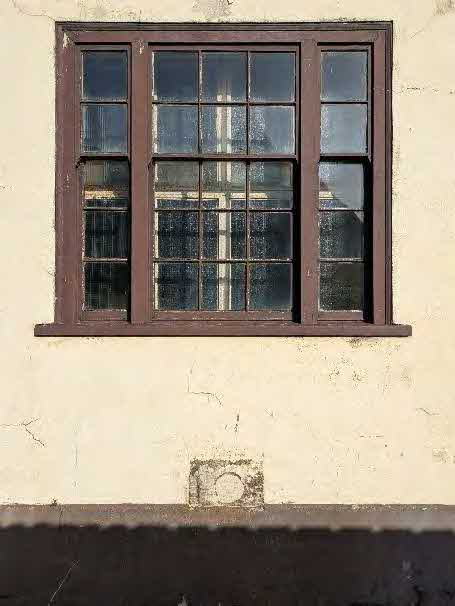 A close-up photograph of a traditional multi-paned sash window set into a weathered, cream-colored rendered wall.