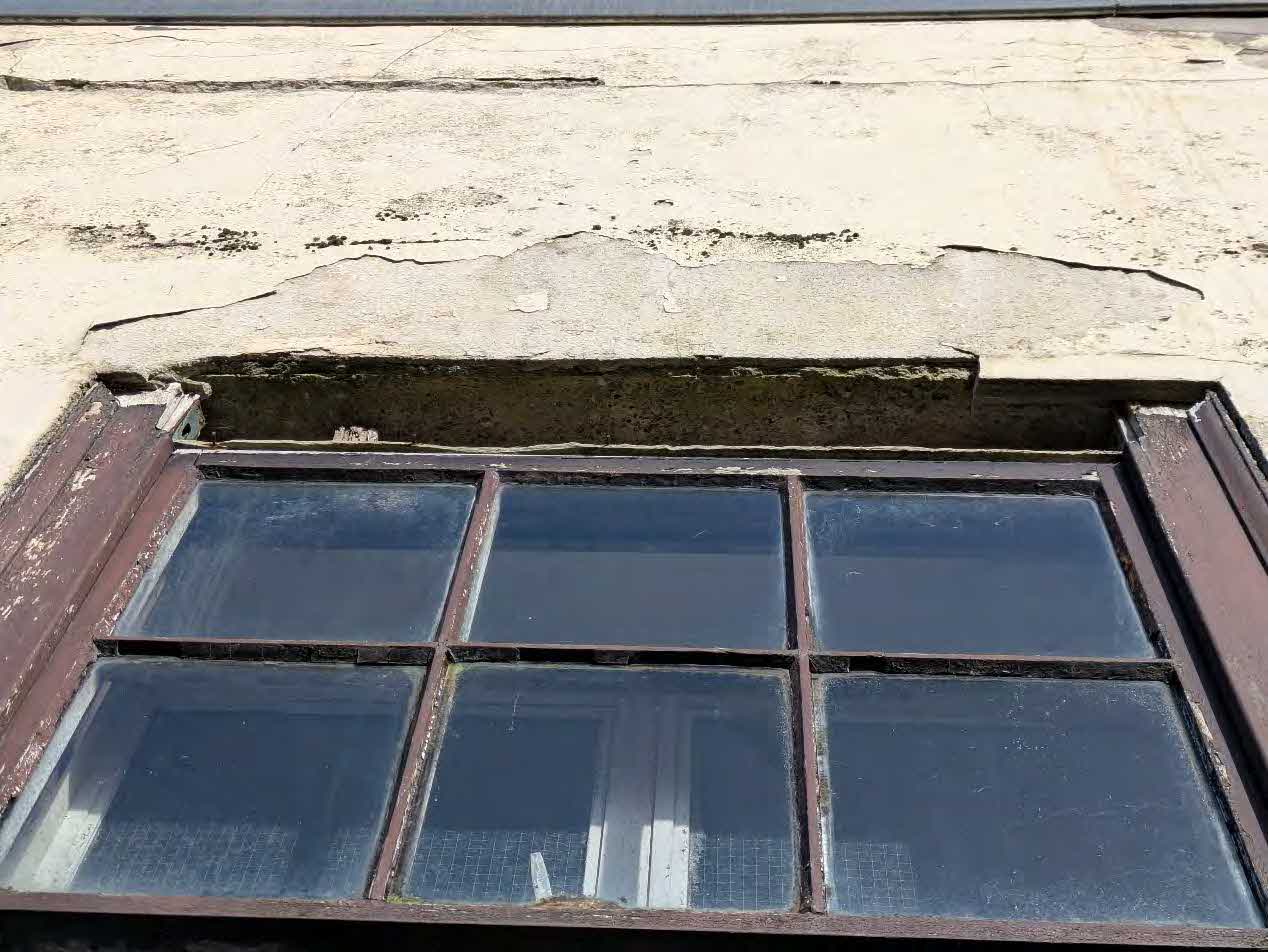 A close-up photograph showing a six-pane window set into a weathered wall with significant horizontal cracking in the render above the frame.