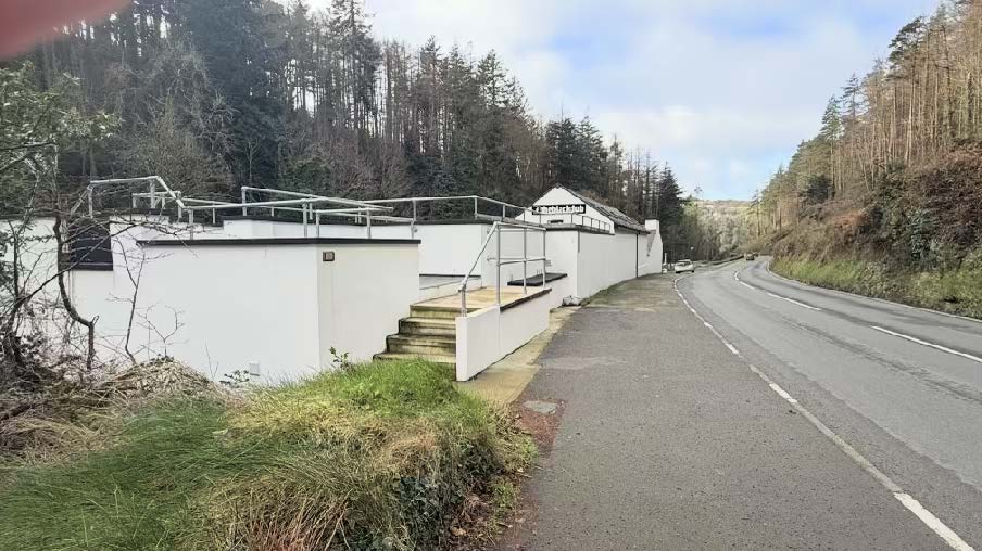 A photograph showing white cladded container structures built into a hillside next to a road, featuring decking and railings.