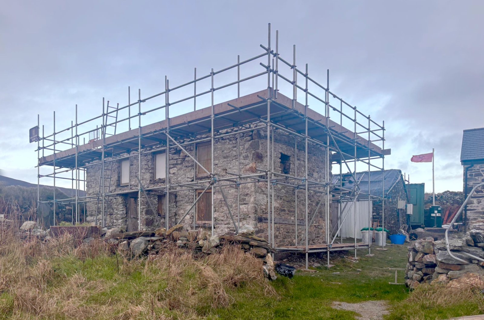 A photograph showing a stone building surrounded by scaffolding, appearing to be under renovation or conversion in a rural landscape.